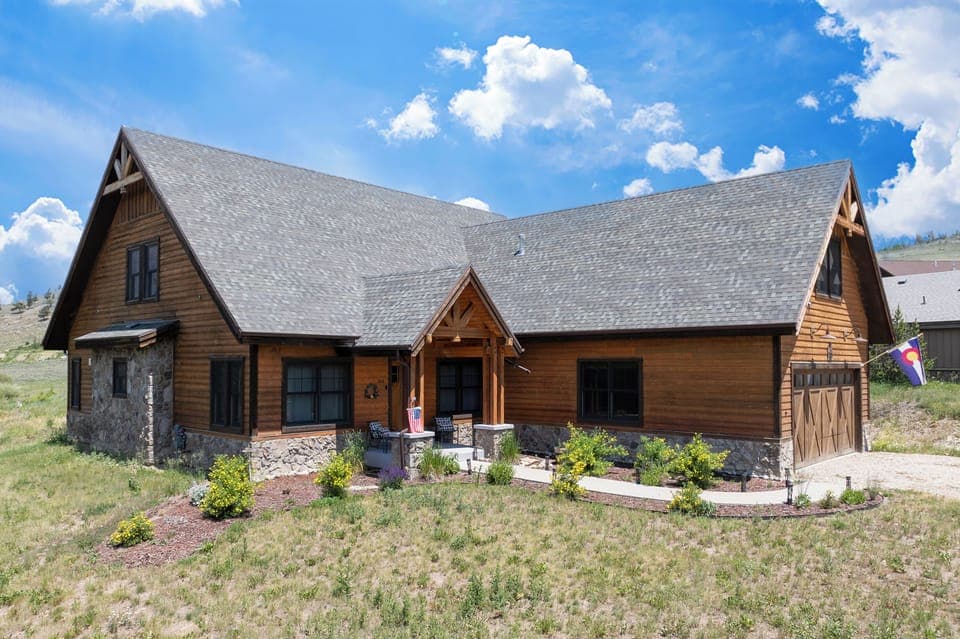 Rustic mountain lodge with stone and timber construction, featuring landscaped grounds and covered entry porch in scenic countryside setting.