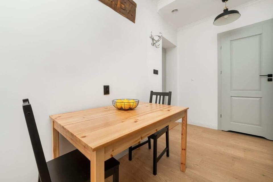 Simple dining area with a wooden table and black chairs, set against a white wall.