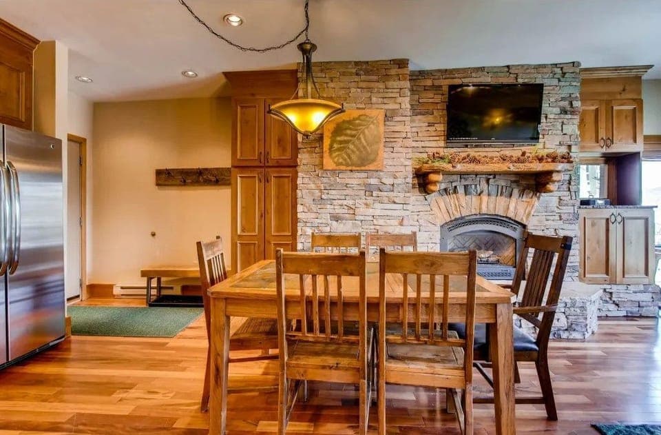 The inviting dining area, adorned with rustic wood furnishings and a cozy stone fireplace, creates a warm ambiance perfect for family meals after a day on the slopes.