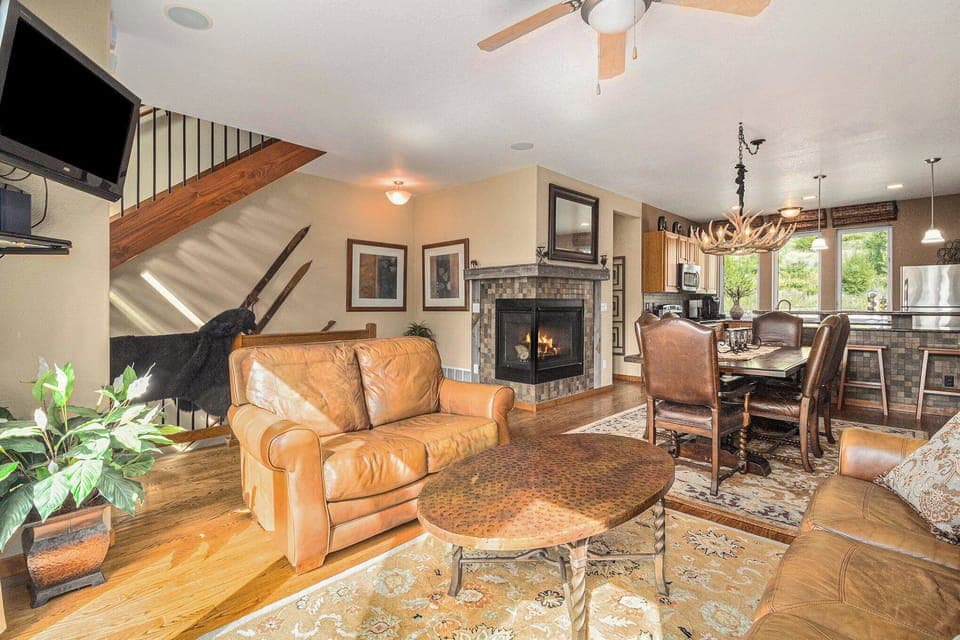 - Warm and inviting living area with leather armchair, fireplace, and rustic charm
- Open concept space flows into dining and kitchen, perfect for entertaining
- Antler chandelier and wood accents add mountain lodge character throughout

