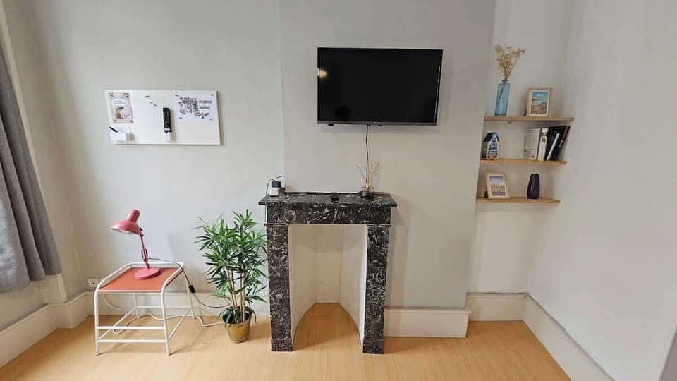 Salon ouvert sur la cuisine, avec canapé convertible pour une personne, télévision et table à manger pour quatre personnes.