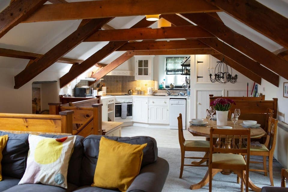 Living/kitchen/diner area: 3 seater sofa with bright coloured cushions, dining table with four chairs leading to fitted kitchen