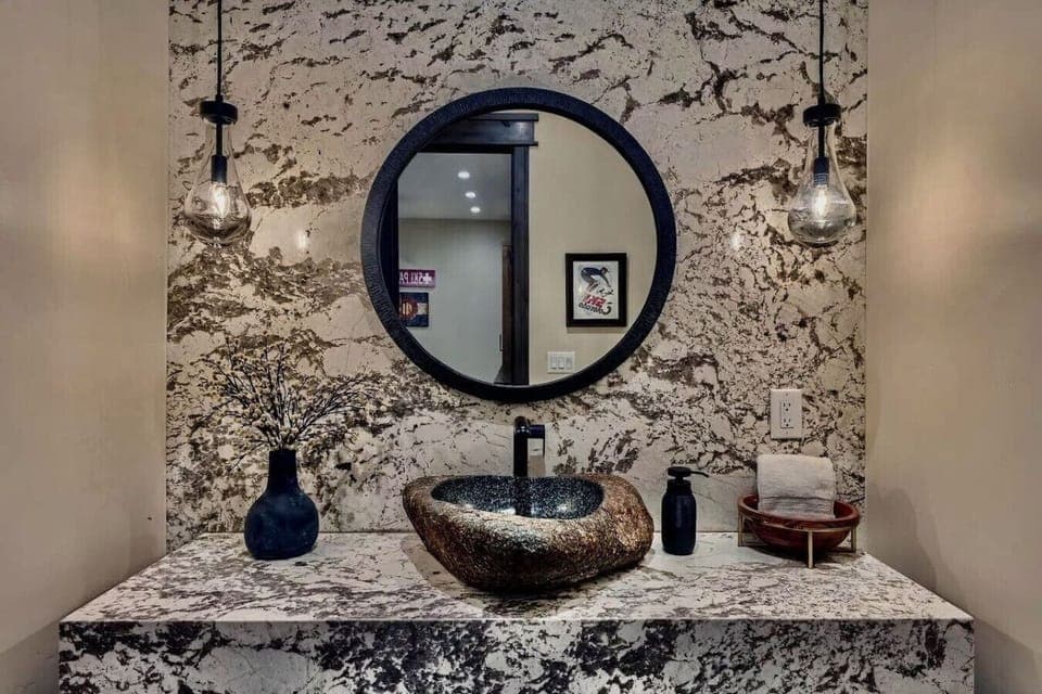 Experience elegance in this modern bathroom with a striking stone sink, chic lighting, and sleek finishes, creating a perfect space for functionality and style.