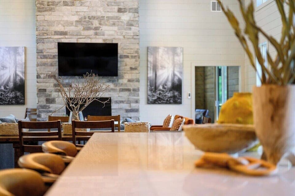 Open concept view of kitchen island and dining area facing stone fireplace and cozy living room.