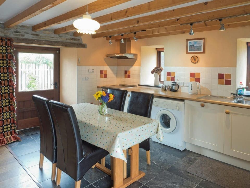 Fitted kitchen/dining area: washing machine, cooker, kettle and sink: dining table with four chairs, two windows and door to patio