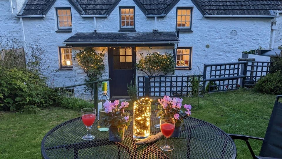 Garden at night with outdoor fairy lights on outdoor table and around cottage entrance