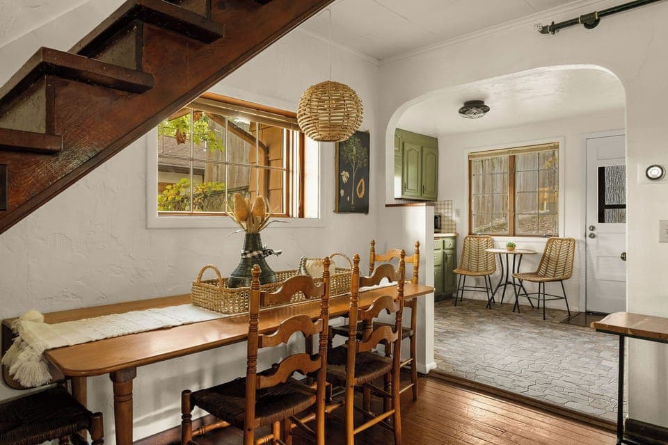 - Enjoy meals in a cozy dining nook tucked under a rustic staircase
- Beautiful natural light and wood textures create a warm ambiance
- Open archway leads to a charming vintage-style kitchen