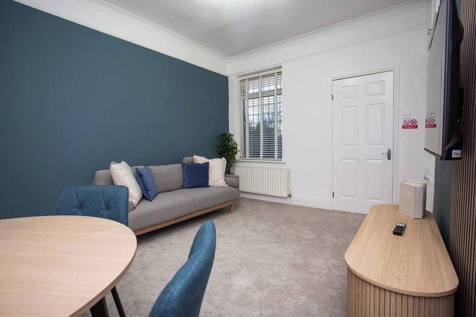 Modern and cozy living space with a stylish blue accent wall, comfortable sofa, dining area, and TV. Bright, inviting, and perfect for relaxation.