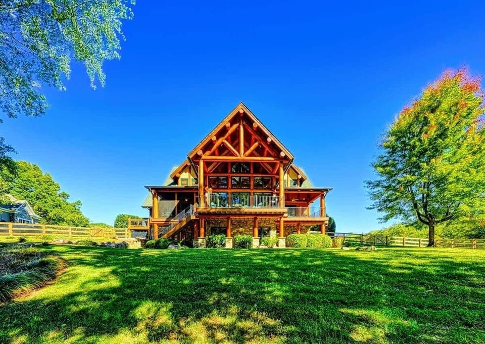 A stunning, spacious log cabin with large windows, surrounded by lush greenery and vibrant blue skies