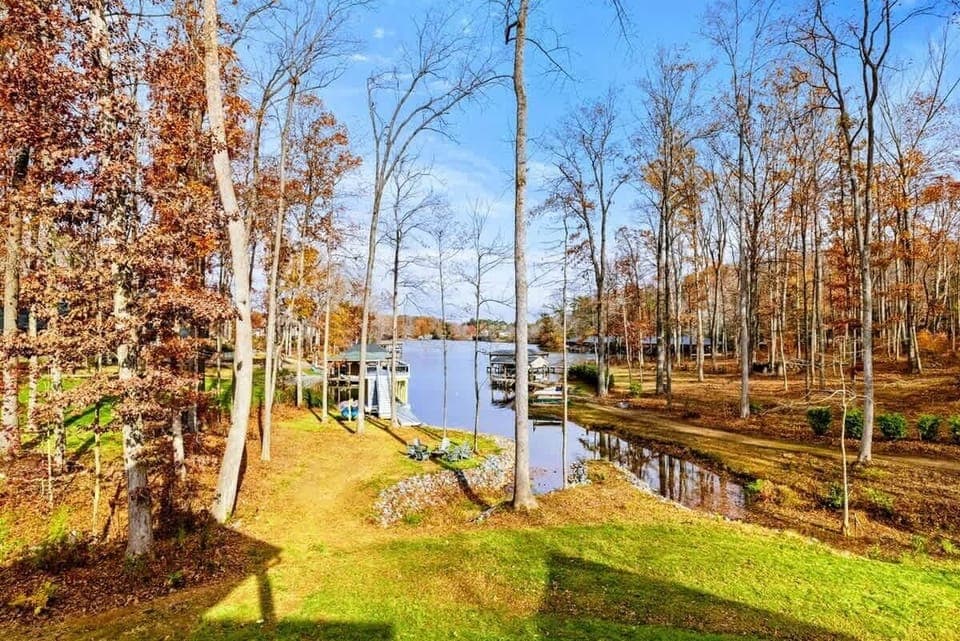 Peaceful lakeside backyard with lush greenery, tall trees, and direct water access surrounded by nature.