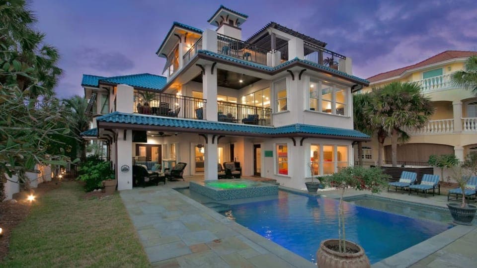Elegant coastal villa features distinctive blue-tile roofing and multi-level architecture, complemented by tropical landscaping and neighboring properties in this desirable area.