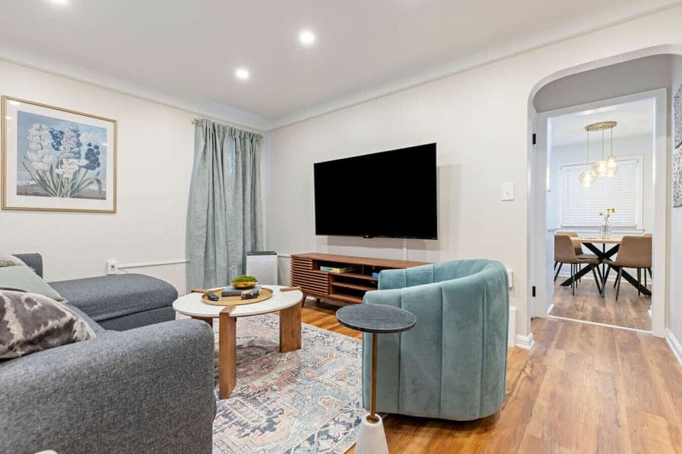 Stylish and cozy living area with a modern aesthetic, featuring plush seating, a large TV, and a peek into the elegant dining space—ideal for relaxing or entertaining.