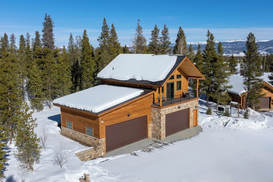 Mountain retreat property nestled among snow-covered evergreens with stunning alpine backdrop and winter wonderland setting.