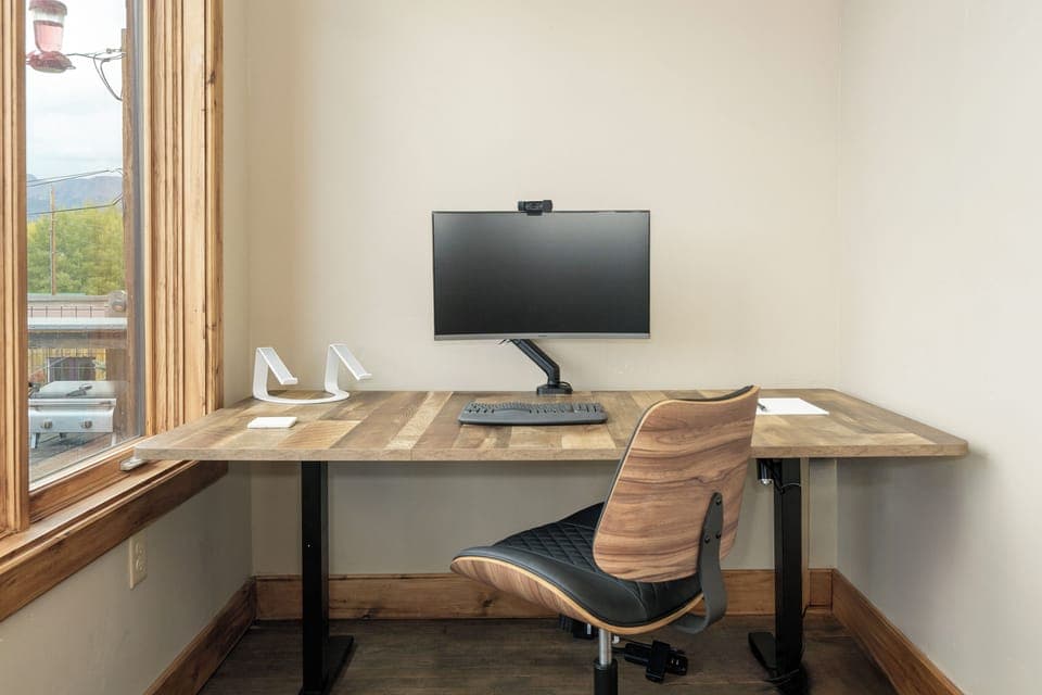 Your dedicated workspace features a sleek desk, ergonomic chair, and mounted monitor—perfect for productive work sessions with natural light streaming in.