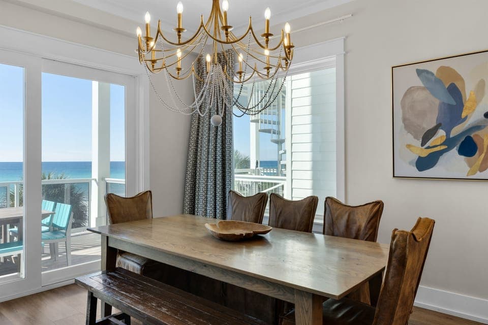 Your elegant dining room flows seamlessly to oceanfront balcony, where golden chandelier light mingles with stunning sea views.