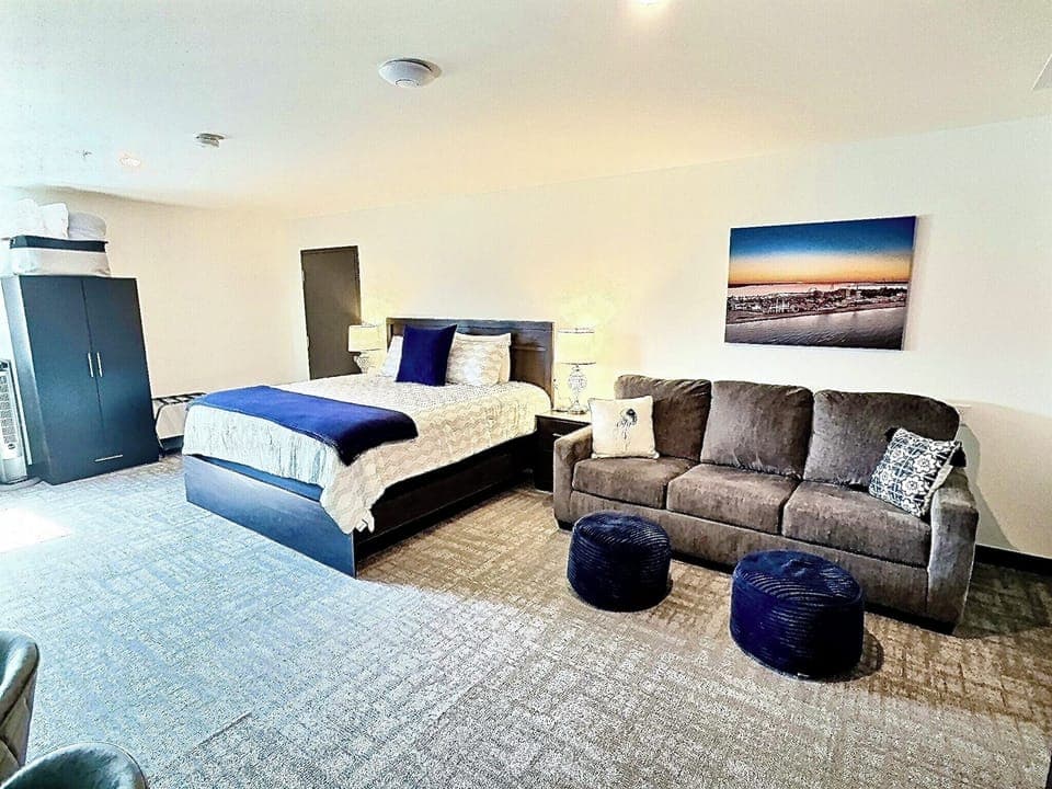 A bright, open room featuring a comfortable bed, work desk, ample storage, and a large TV, perfect for relaxing or working during your stay.