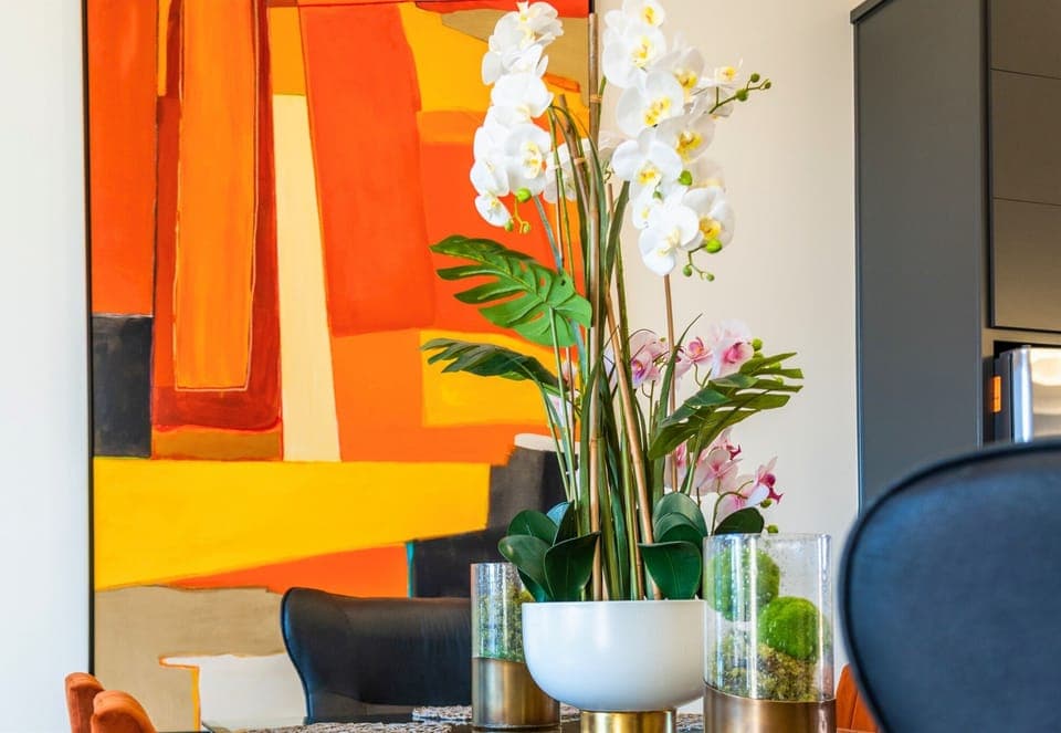 This dining area comes alive with bold, vibrant artwork, a stunning floral centerpiece, and an effortlessly modern yet welcoming ambiance for every gathering.