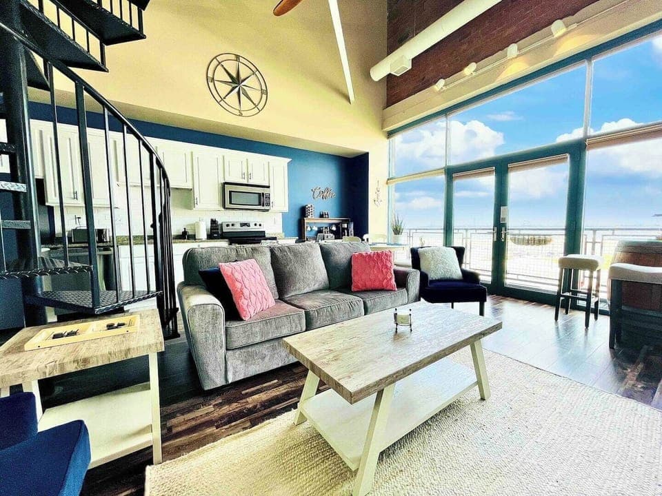 Spacious and stylish living room featuring a spiral staircase, open kitchen layout, and floor-to-ceiling windows that flood the space with natural light.