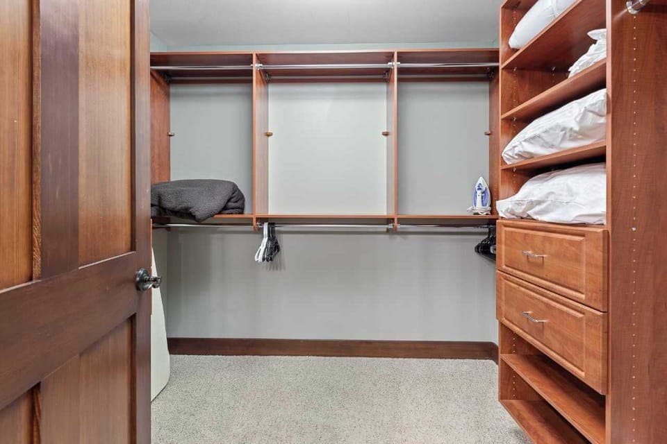 Primary bedroom walk in closet with iron and ironing board.