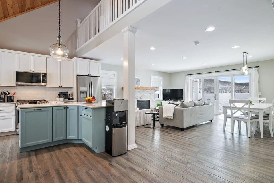 Welcome to this inviting lakeside escape! The open-concept layout seamlessly blends a chic kitchen with soft blue cabinets, stainless-steel appliances, and a cozy dining nook.