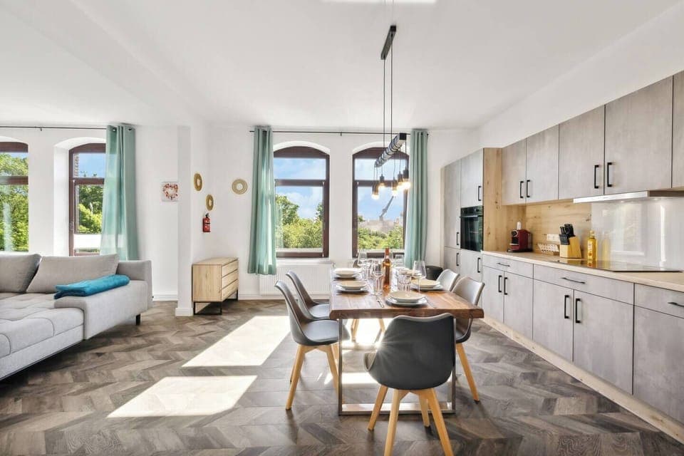Offene Wohnküche mit modernem Esstisch, stilvoller Beleuchtung und großen Fenstern, die viel Tageslicht hereinlassen.