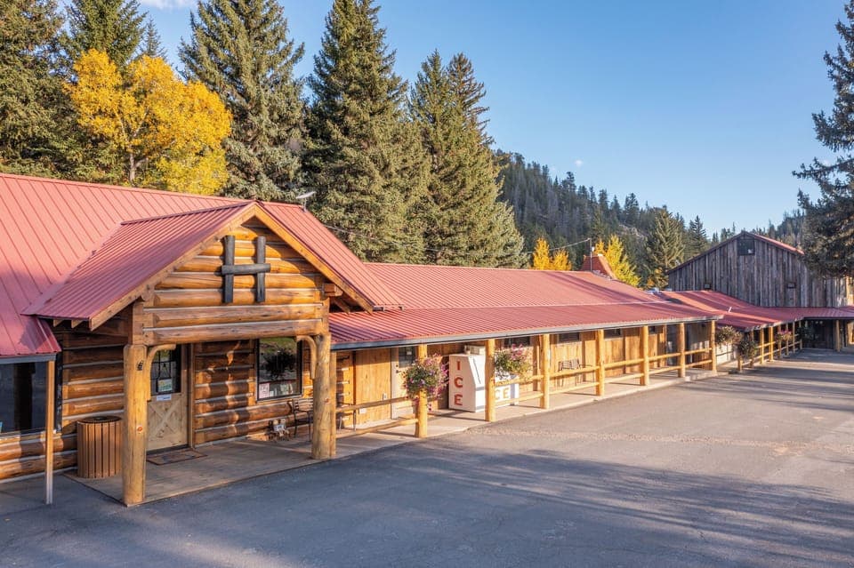Arrive to a cozy lodge entrance framed by pines.