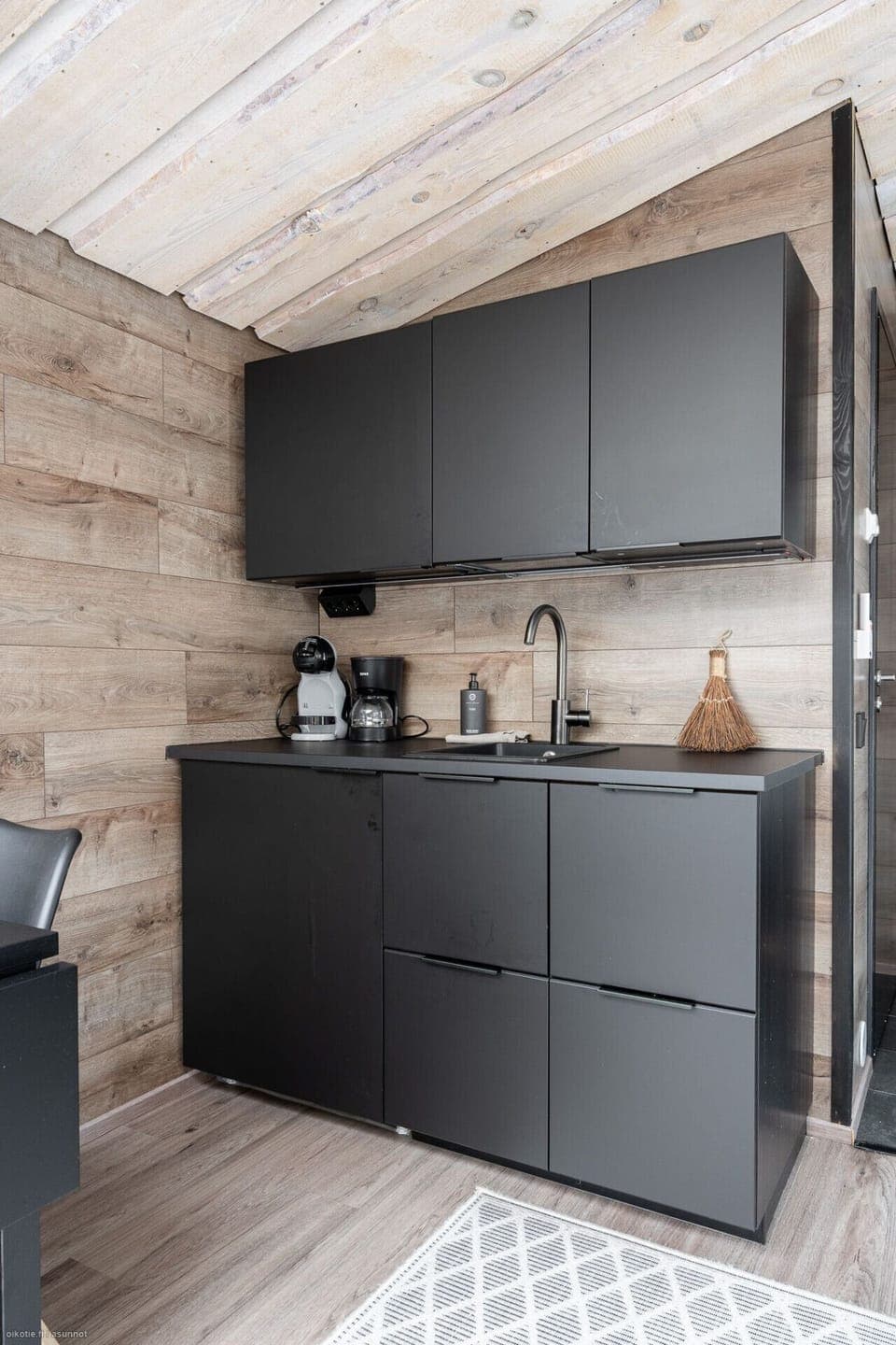 A modern, compact kitchenette provides everything you need for a comfortable stay, including a coffee maker and a Nespresso machine. The sleek, black design beautifully complements the warm wood paneling, offering a stylish and convenient space for prepar