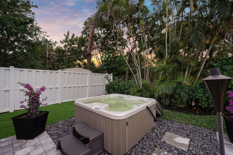 Unwind in your private backyard oasis featuring a cozy hot tub, lush greenery, and soft outdoor lighting. The perfect spot to relax after a long day.