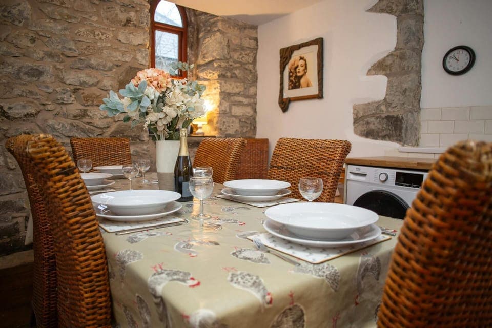 Rustic dining room with stone walls, set table and vase of flowers under a small window