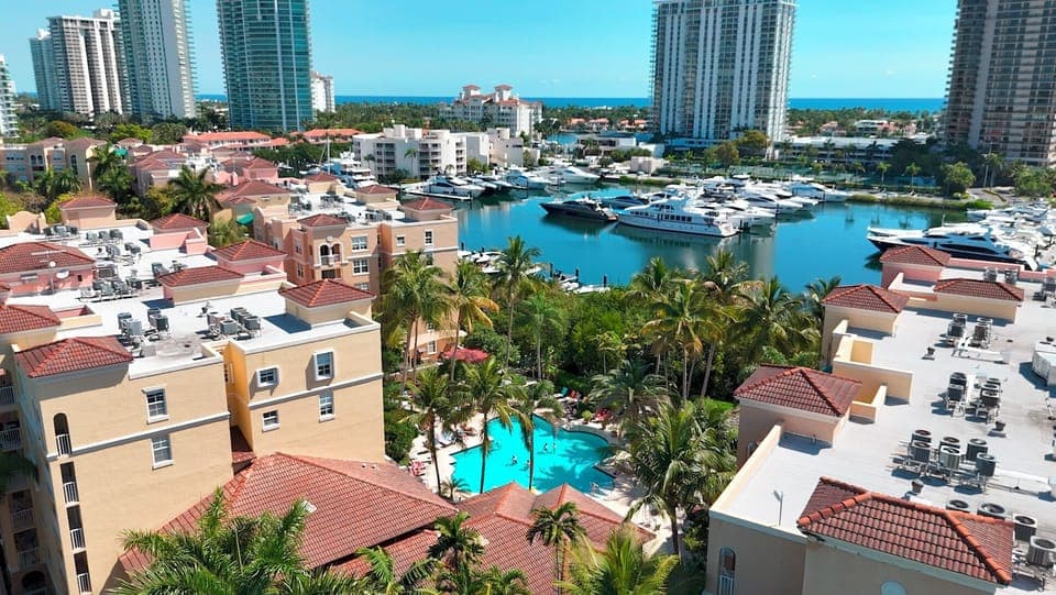 Vibrant marina scene with yachts, palms, and a turquoise pool below