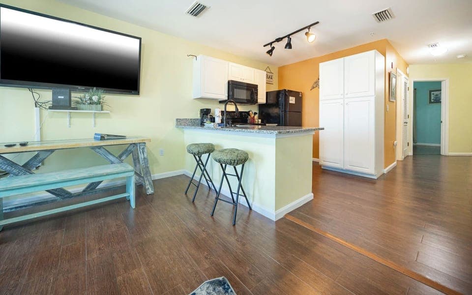 The living area features a large TV, a stylish bar with seating, and a well-equipped kitchen with granite countertops