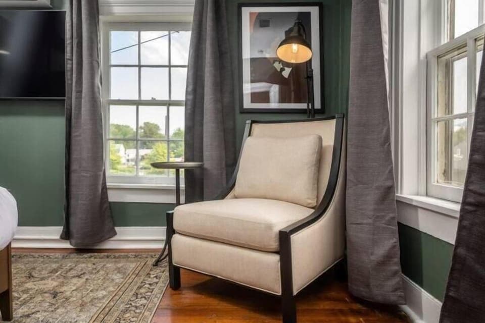 Sunlit reading nook w/ cozy armchair & tall windows overlooking the grounds