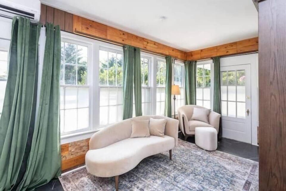 Sunlit sitting room w/ curved sofa, cozy chairs & windows wrapping the space in natural light