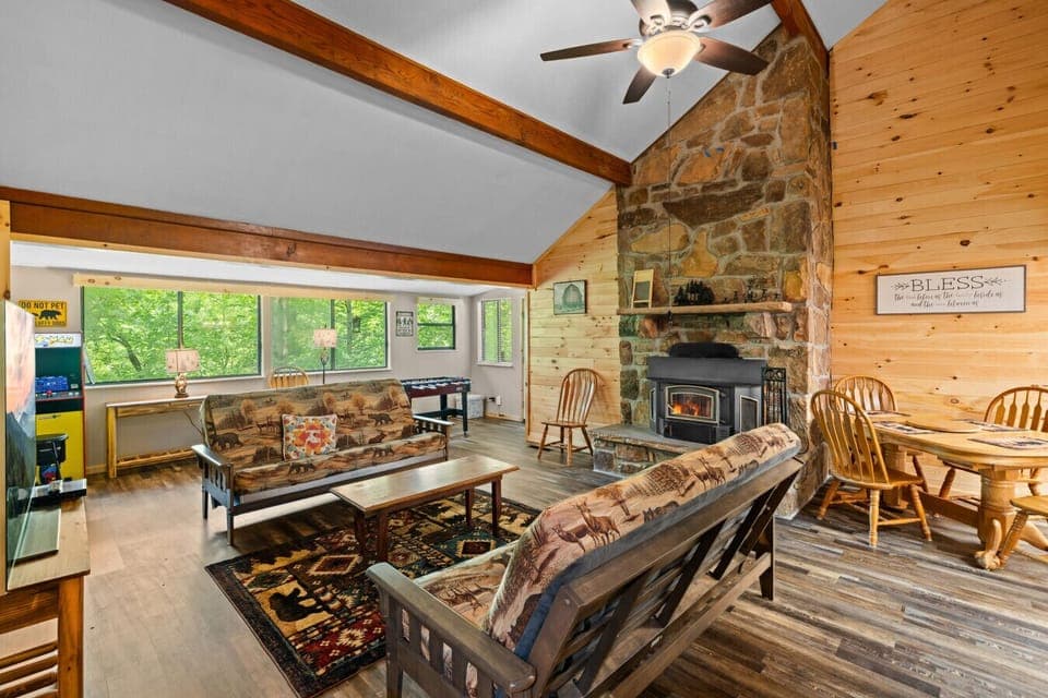 Gather around the crackling wood stove in this cozy living space, where tall ceilings, warm wood walls, and woodland decor invite you to truly unwind.