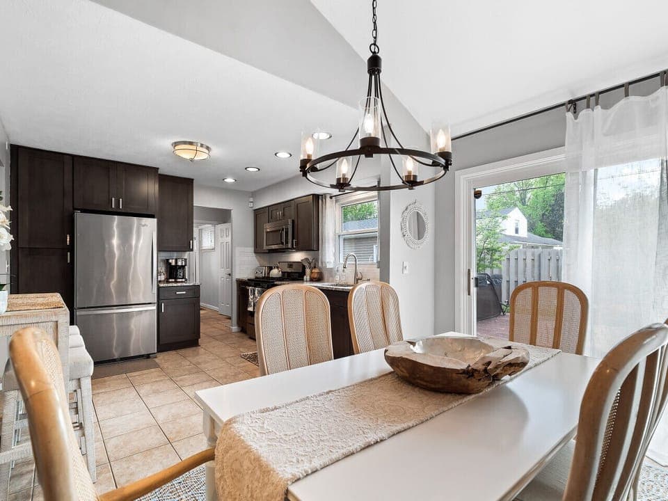 Elegant dining space with seating for six 🍽️, set beneath a statement chandelier 💡. Natural light flows in through sheer curtains, creating a bright and welcoming area for meals, games, or conversation 🌞.