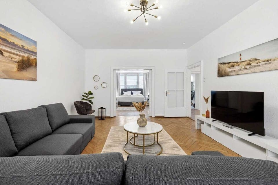 Großzügiges Wohnzimmer mit moderner Einrichtung und Blick ins Schlafzimmer.