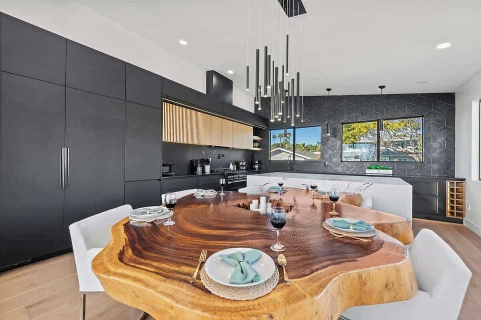 A live-edge table takes center stage, complemented by contemporary seating and minimalist lighting. Black cabinetry with fluted wood-finished cupboards and wood-designed floors create a warm yet modern atmosphere. 