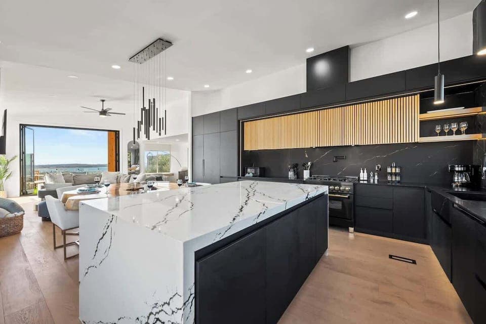 This 2,804 sq ft property boasts an organic modern opulence warmed with natural wood and stone accents. Here it shows how bold black cabinetry, warm natural wood, and a sleek white waterfall island come together to create the perfect modern kitchen. 