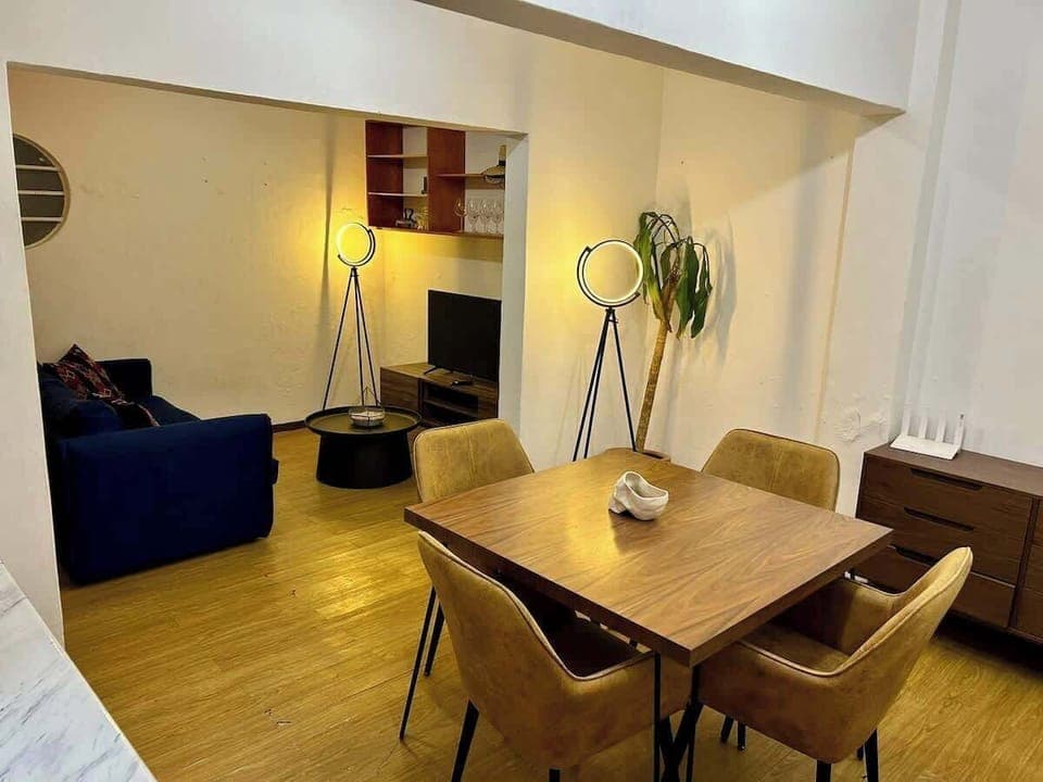 Comedor (mesa con 4 sillas, cocina integrada, planta de decoración, sala de entretenimiento al fondo)