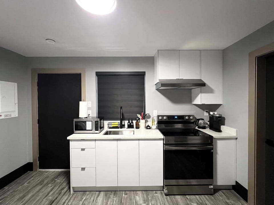 This photo showcases the functional side of the kitchen area, featuring a stacked washer and dryer unit next to the dining table. The kitchen counter with a sink and the entrance to another room are also visible, emphasizing the space's convenience.