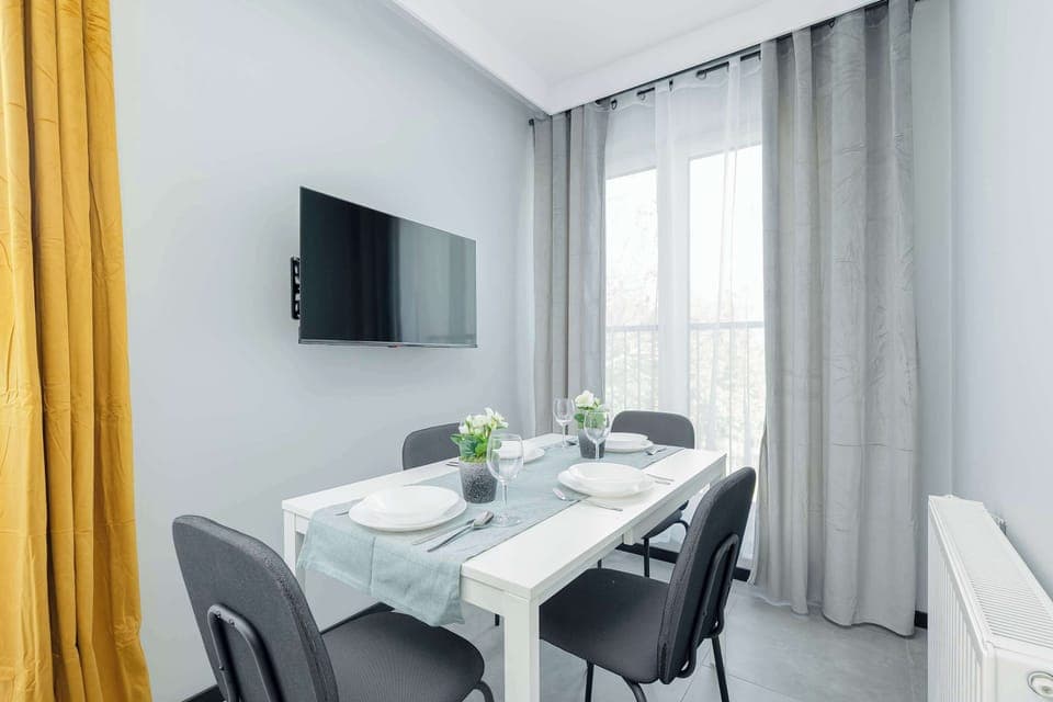 An elegant dining room with a white table, four stylish chairs and yellow and grey curtains provides a pleasant place to share meals.