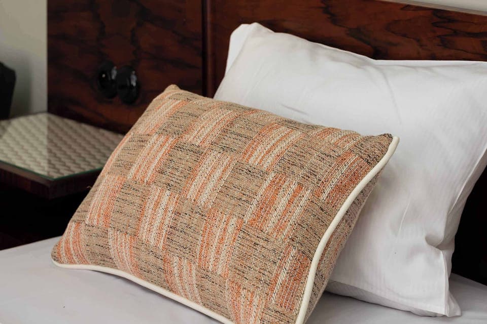 A close-up of a bed corner, showcasing a textured, patterned pillow on crisp white bedding.
