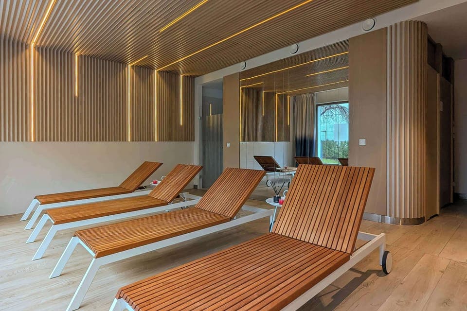 The interior of the relaxation area, with its wooden loungers, illuminated lamella ceiling and mirrored wall, creates a calm and modern space for relaxation.