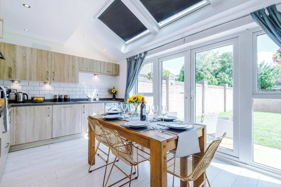 Bright, modern kitchen with full appliances, stylish wood cabinetry, and a spacious dining area. Enjoy meals at the rustic table with views of the garden through large French doors. Perfect for cooking, dining, and gathering.