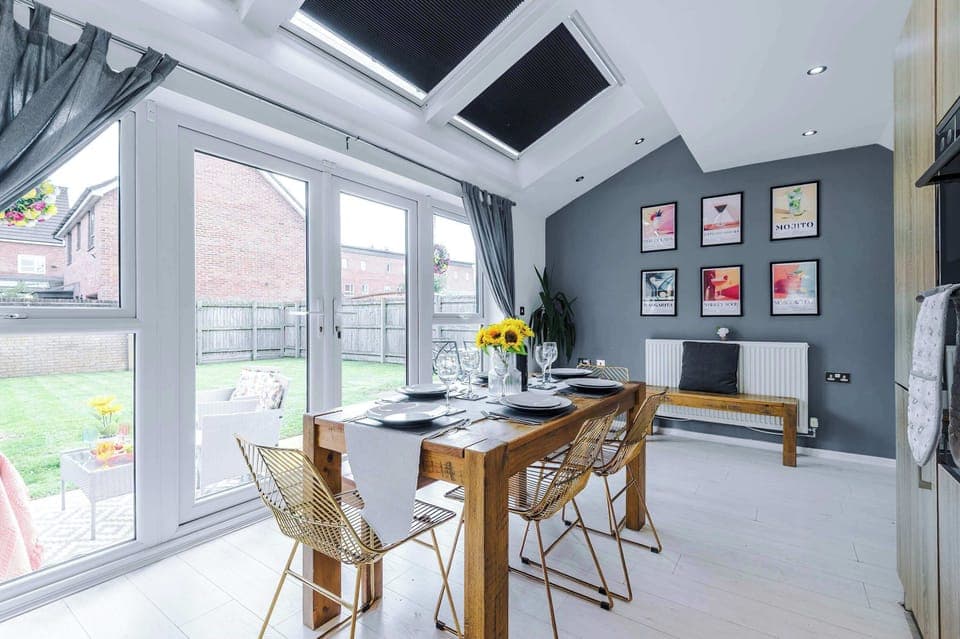 Bright, modern kitchen with full appliances, stylish wood cabinetry, and a spacious dining area. Enjoy meals at the rustic table with views of the garden through large French doors. Perfect for cooking, dining, and gathering.