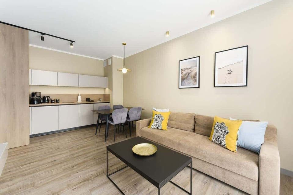 A bright open-plan living area with a sofa, a coffee table, and a small kitchen corner, designed for relaxation and functionality.
