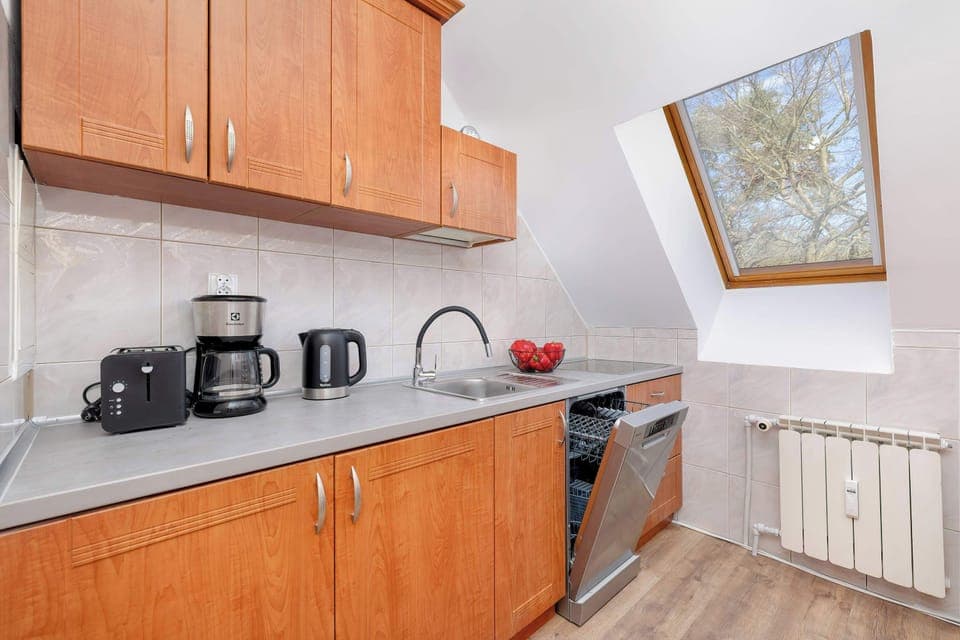 A traditional-style kitchen with wooden cabinets, white countertops, and modern appliances, including a kettle and coffee maker.