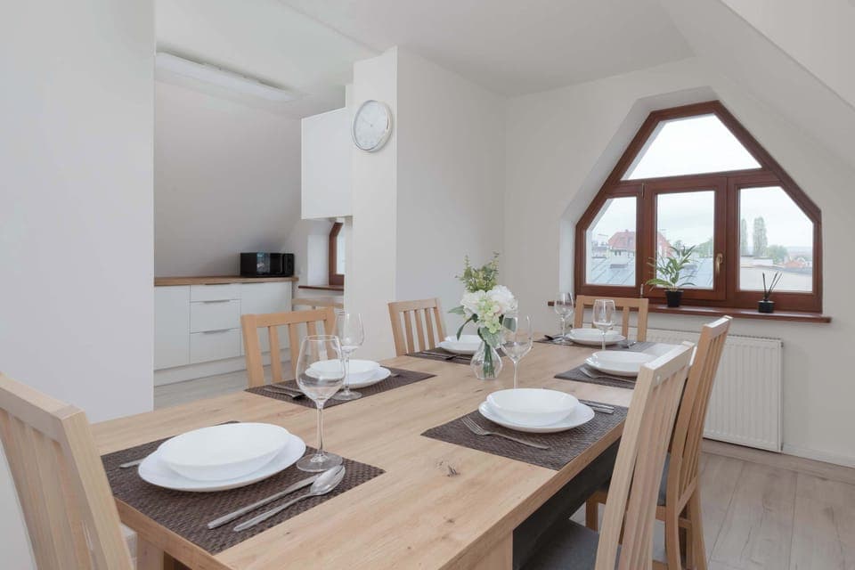 A wooden table, with six chairs and a cover, located in a bright dining room with a view of the surrounding area.