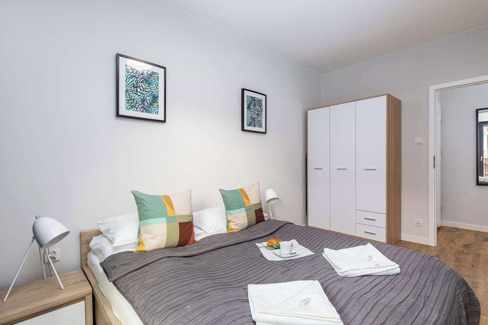 A comfortable bedroom with a double bed with decorative pillows and a large white wardrobe that provides space for storing personal belongings.