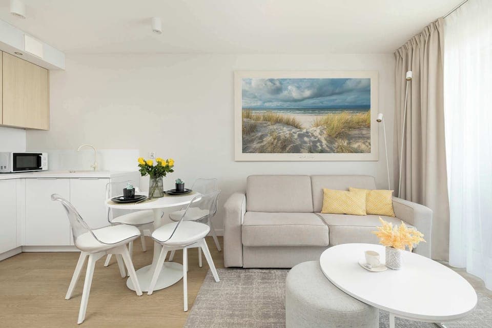 A bright living room with a comfortable sofa, coffee table, and dining space. Large windows let in plenty of natural light.